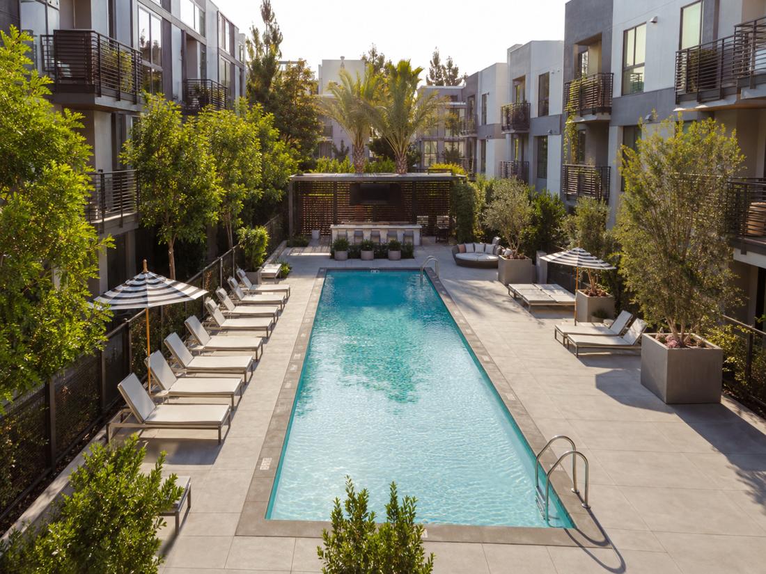 A modern apartment courtyard pool lined with lounge chairs and balconies
